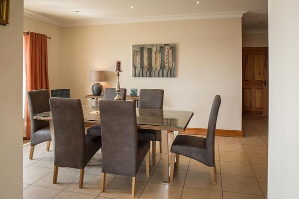 Un coin repas avec une table en verre et quatre chaises, une lampe et un tableau au mur.