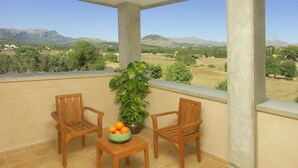 A balcony with two wooden chairs, a small table, and a bowl of oranges. A potted plant is also visible.