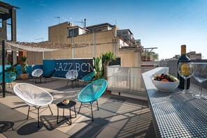Terraza en la azotea con mesas al aire libre, zona de bar y vistas del edificio llamado 'JAZZ BCN'.