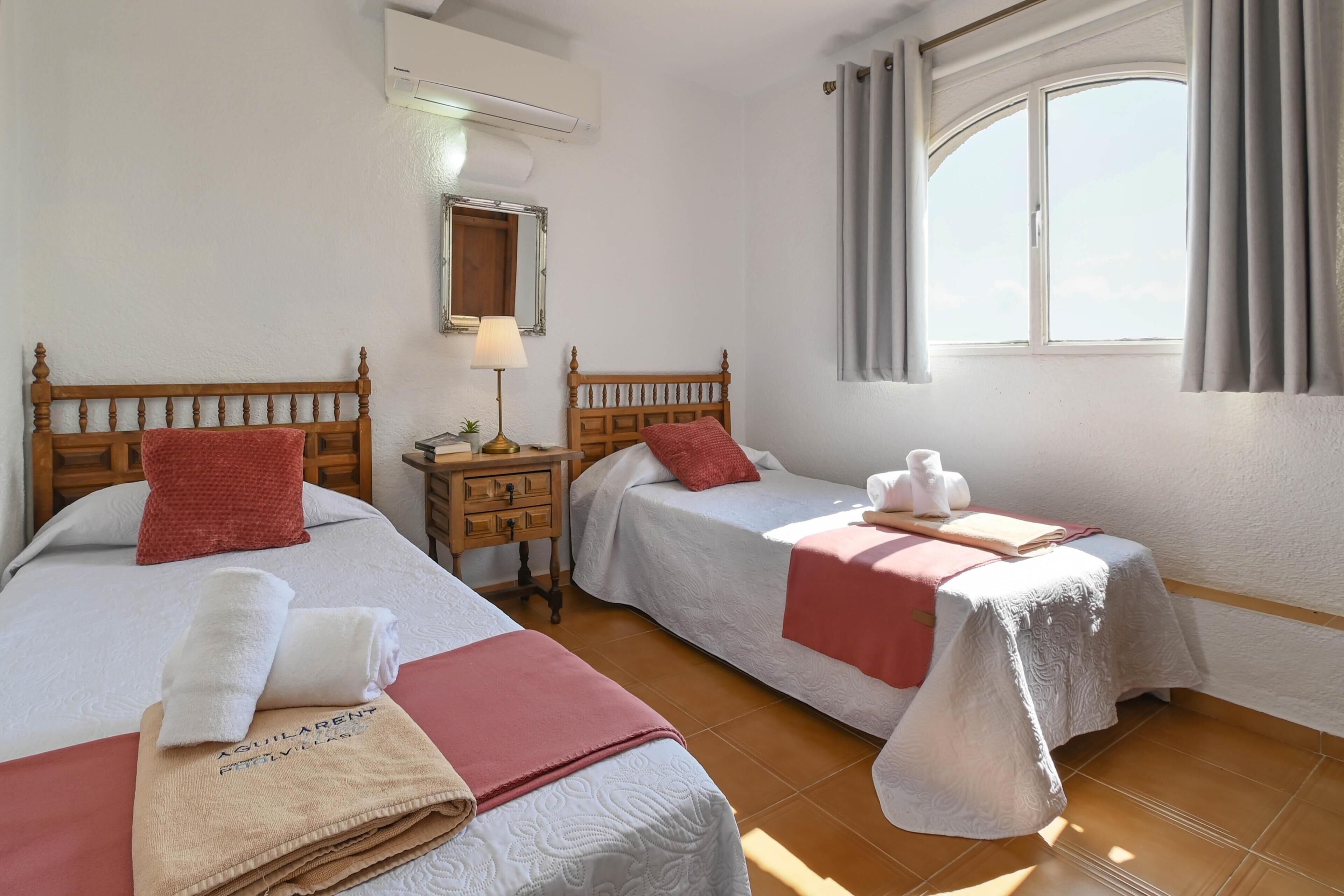 Habitación de hotel con dos camas, una mesita de noche, una lámpara, un espejo y una ventana con cortinas.