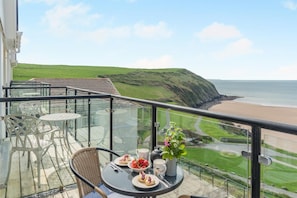 A balcony with a table set for two, overlooking a beach and green landscape. - 2 Bed in Putsborough (oc-flat31) (Croyde)