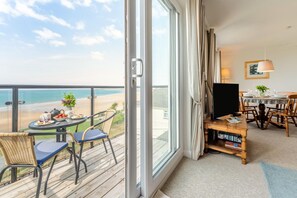 A balcony with a table set for breakfast, a TV, and a dining area with chairs and a table. - 2 Bed in Putsborough (oc-flat31) (Croyde)