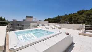 Un espace piscine aménagé sur le toit, avec un jacuzzi, des chaises longues et une vue sur le paysage environnant.