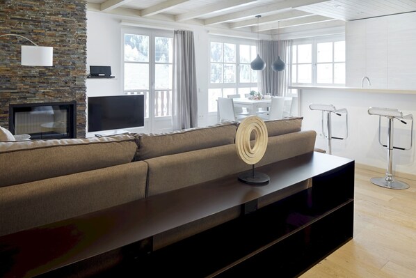 Un salon moderne avec un mur en pierre, un téléviseur à écran plat, un canapé, une table basse et un coin repas avec une table et des chaises blanches.