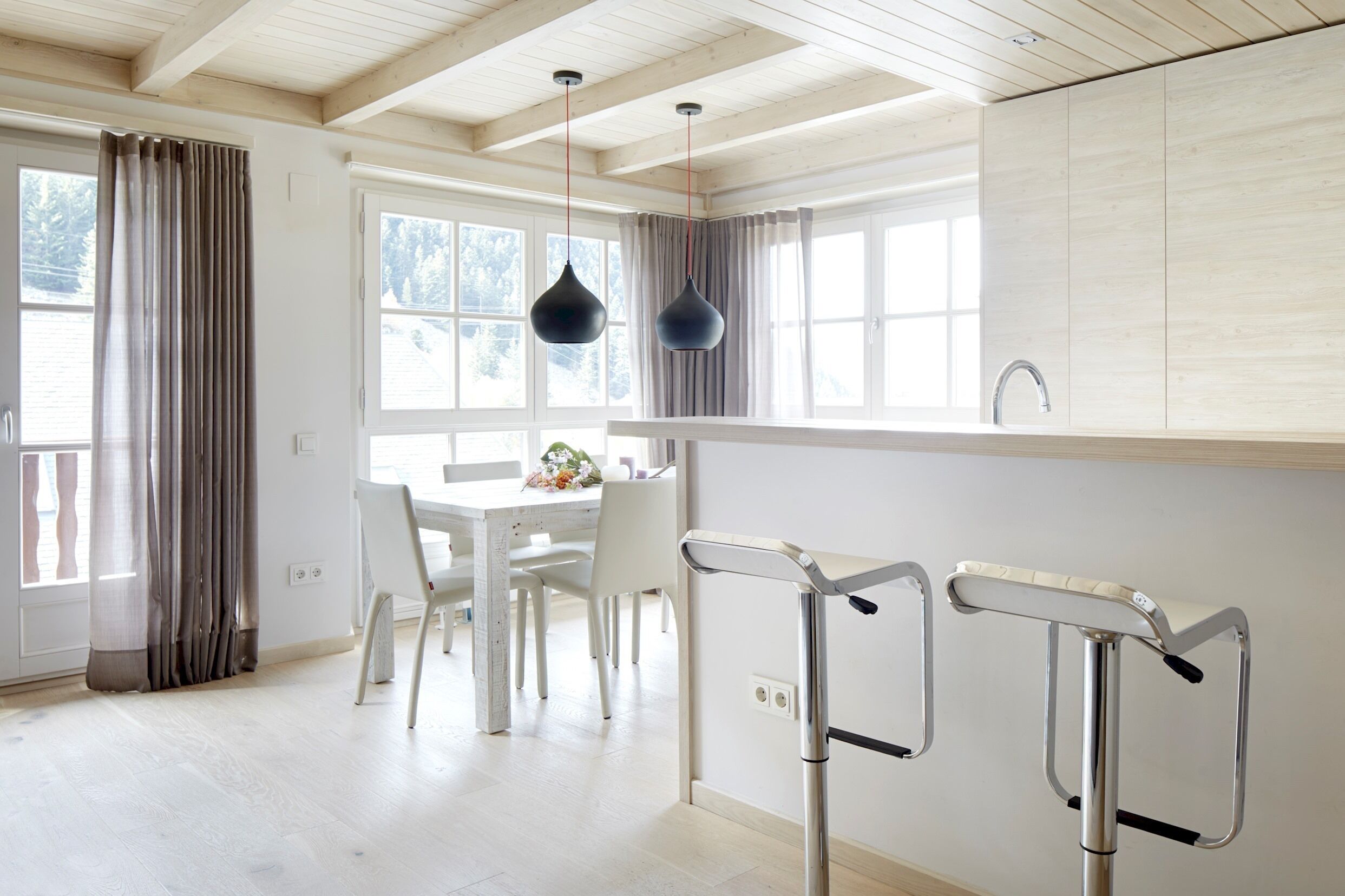 A modern kitchen with white cabinets, a dining area with a white table and chairs, and a window with curtains.