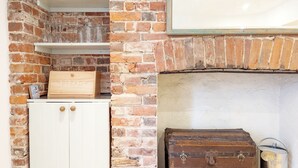 A rustic room with exposed brick walls, a white cabinet, a wooden box labeled 'BREAKFAST', and a vintage trunk. - Dolphin House, Emsworth -  a flat that sleeps 2 guests  in 1 bedroom (Emsworth)