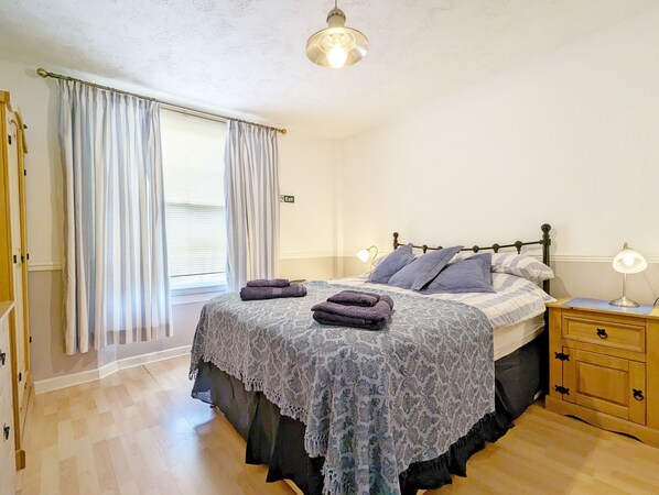 A bedroom with a bed, a nightstand, a lamp, and a window with curtains. - Dolphin House, Emsworth - a flat that sleeps 2 guests in 1 bedroom (Emsworth)
