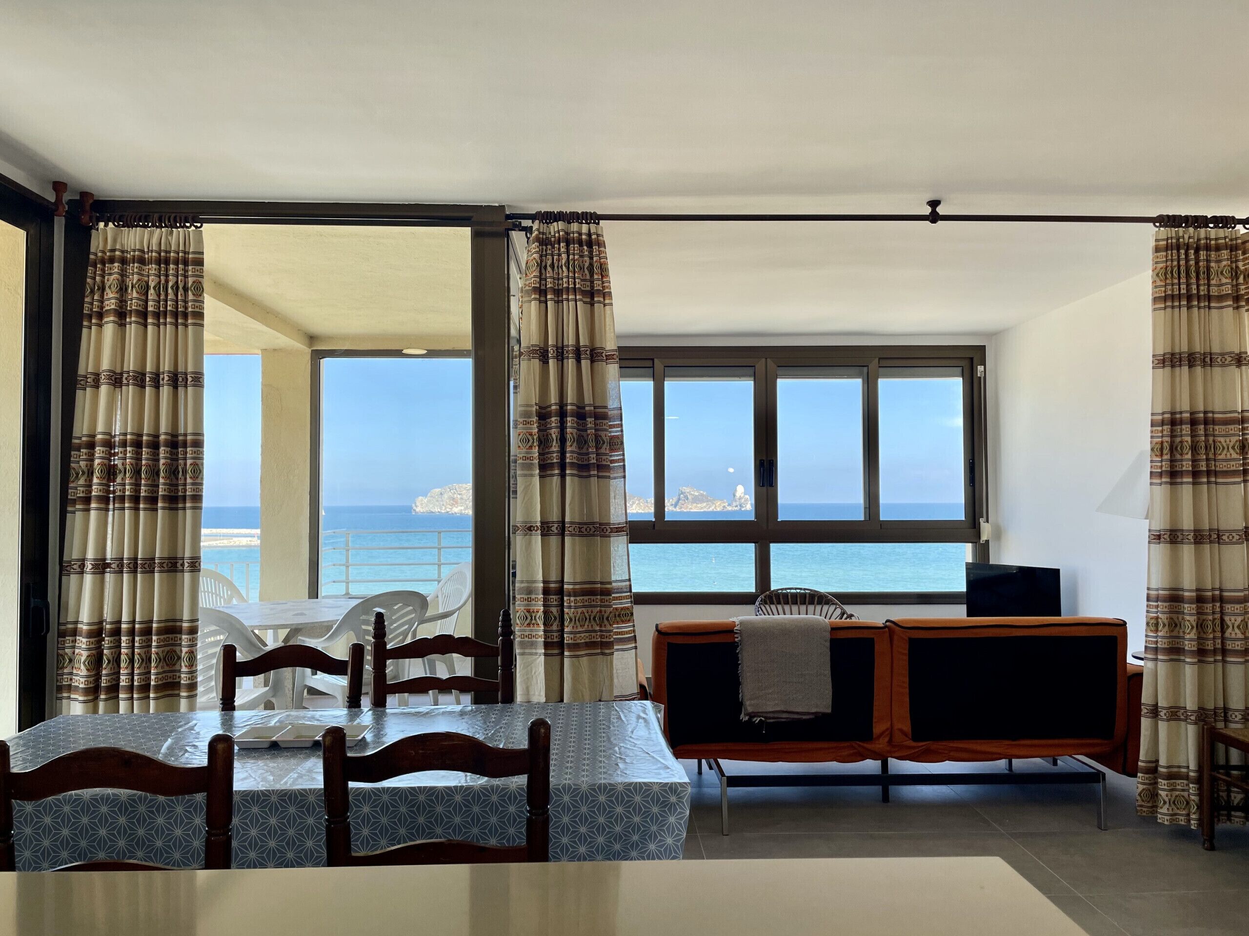 Une pièce comprenant une table à manger, des chaises, un canapé, un téléviseur et offrant une vue sur la mer.