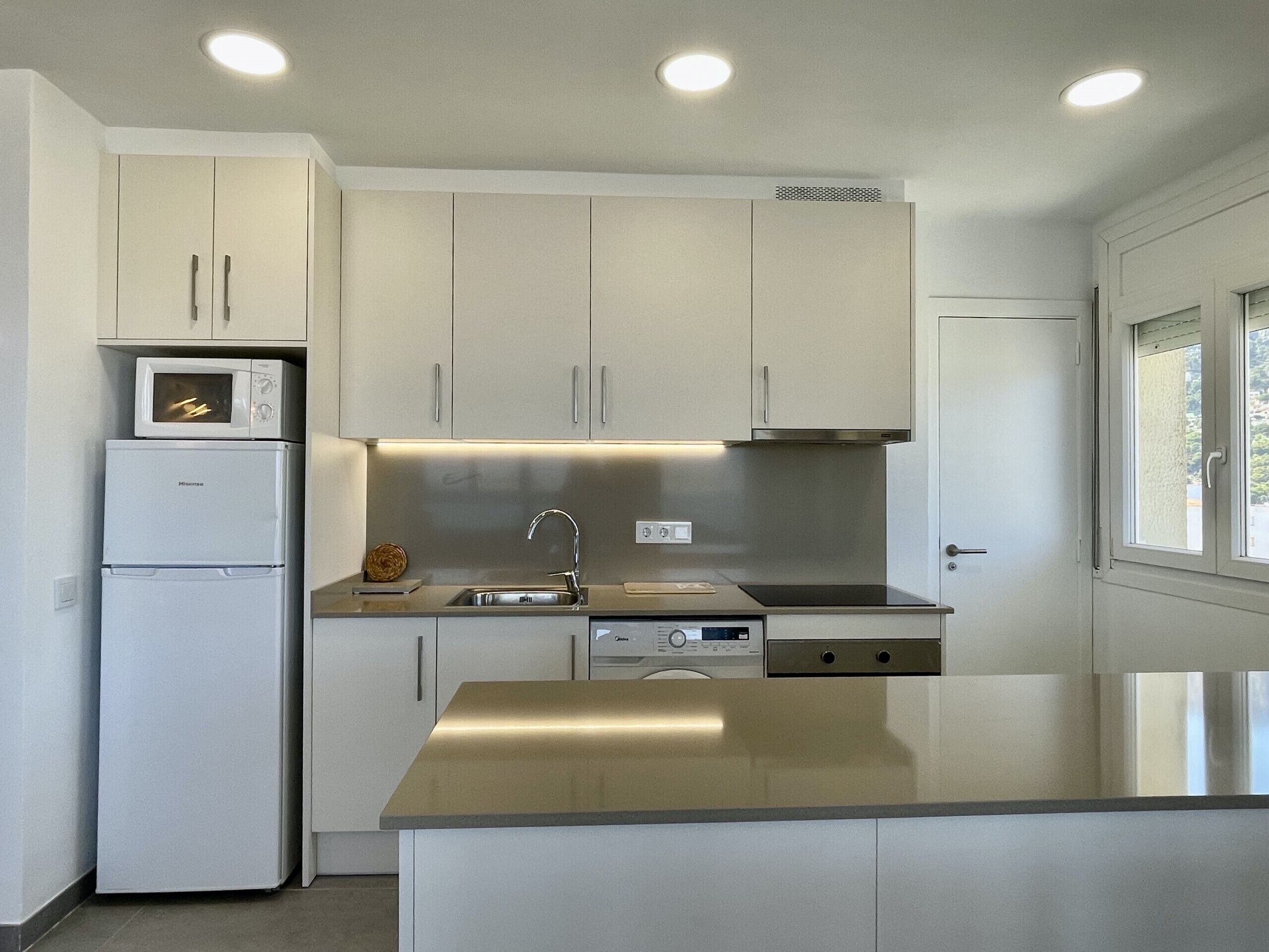A modern kitchen with white cabinets, a built-in microwave, a stainless steel sink, and a dishwasher.