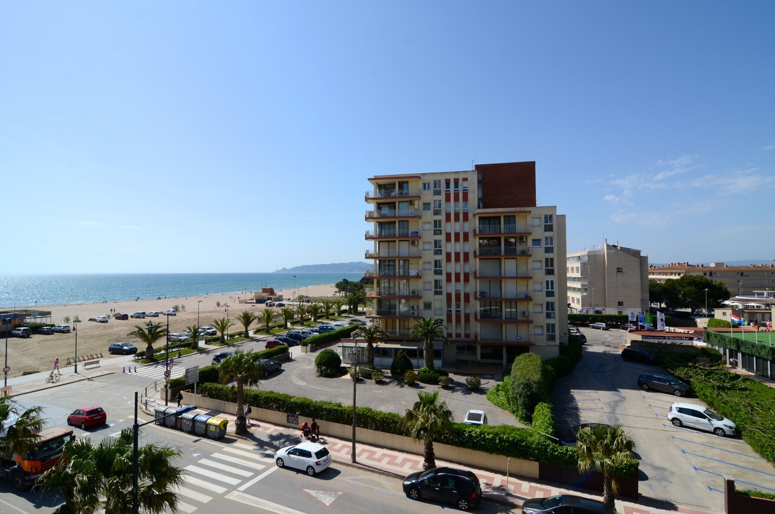 A multi-story building with a beach view, parking area, and palm trees.