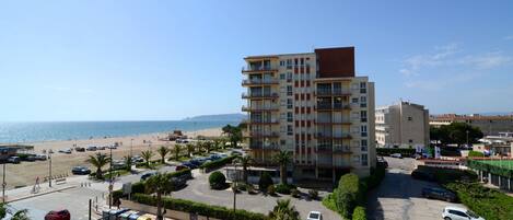 A multi-story building with a beach view, parking area, and palm trees.