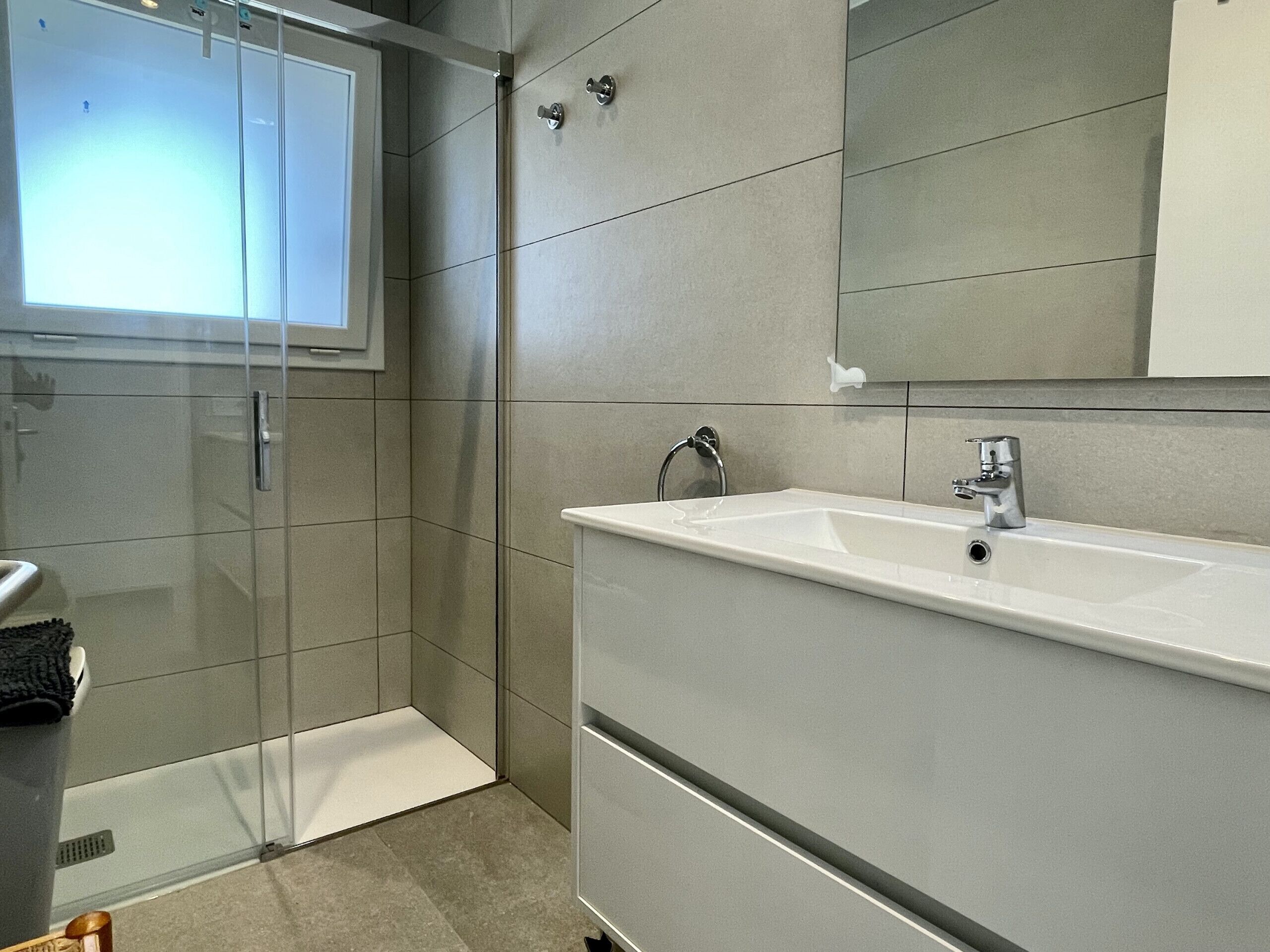 A modern bathroom with a glass shower enclosure, a white sink, and a large mirror.