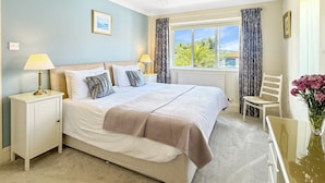 A neatly arranged bedroom with a large bed, bedside lamps, a chair, and a window with curtains. - The Pippins, Old Cleeve (Minehead)