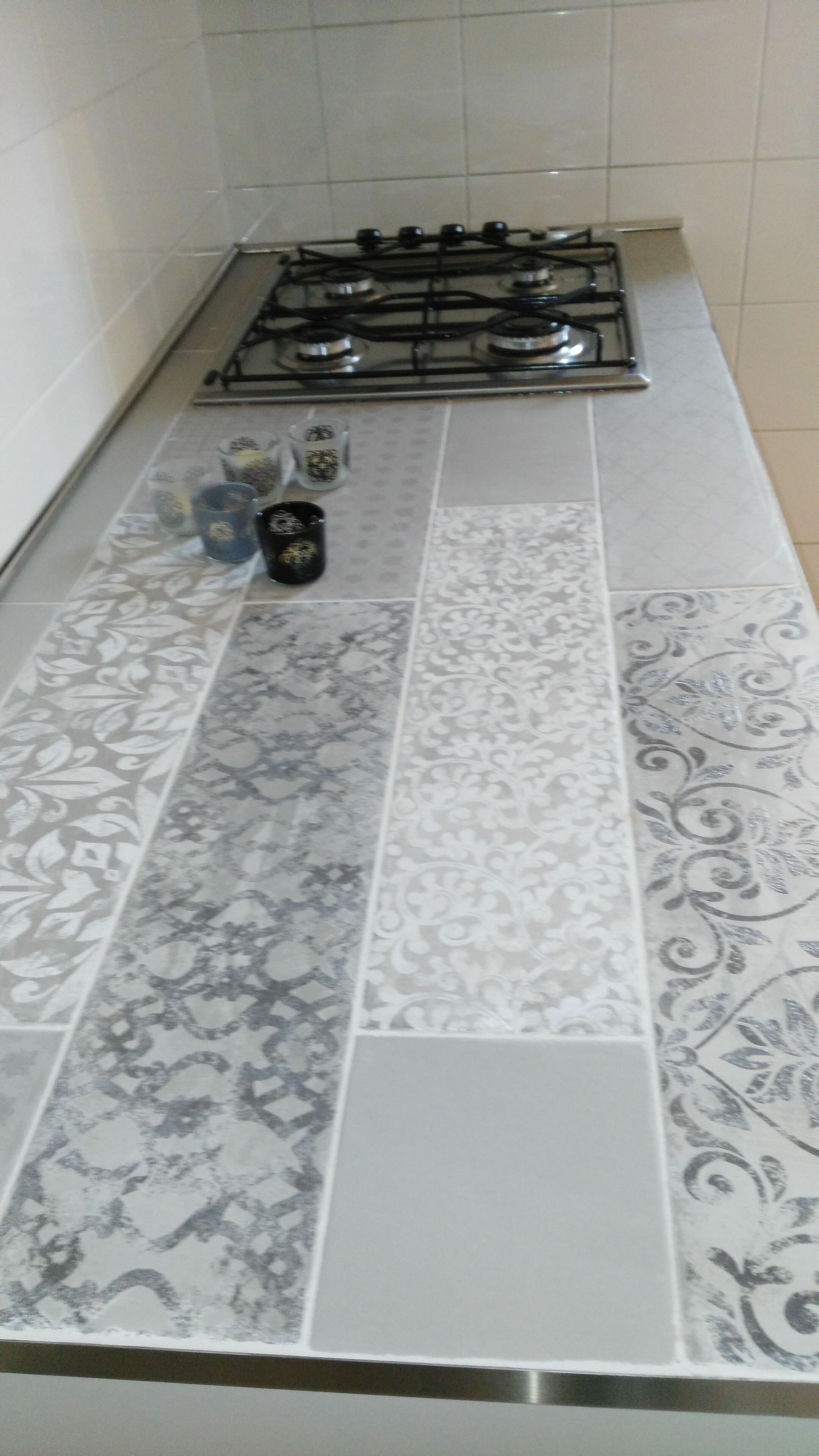Une cuisine avec des carreaux décoratifs, une cuisinière à gaz et quelques tasses posées sur le comptoir.