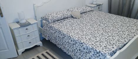 A neatly made bed with a patterned bedspread and pillows, a bedside table with a lamp, and a striped rug on the floor.