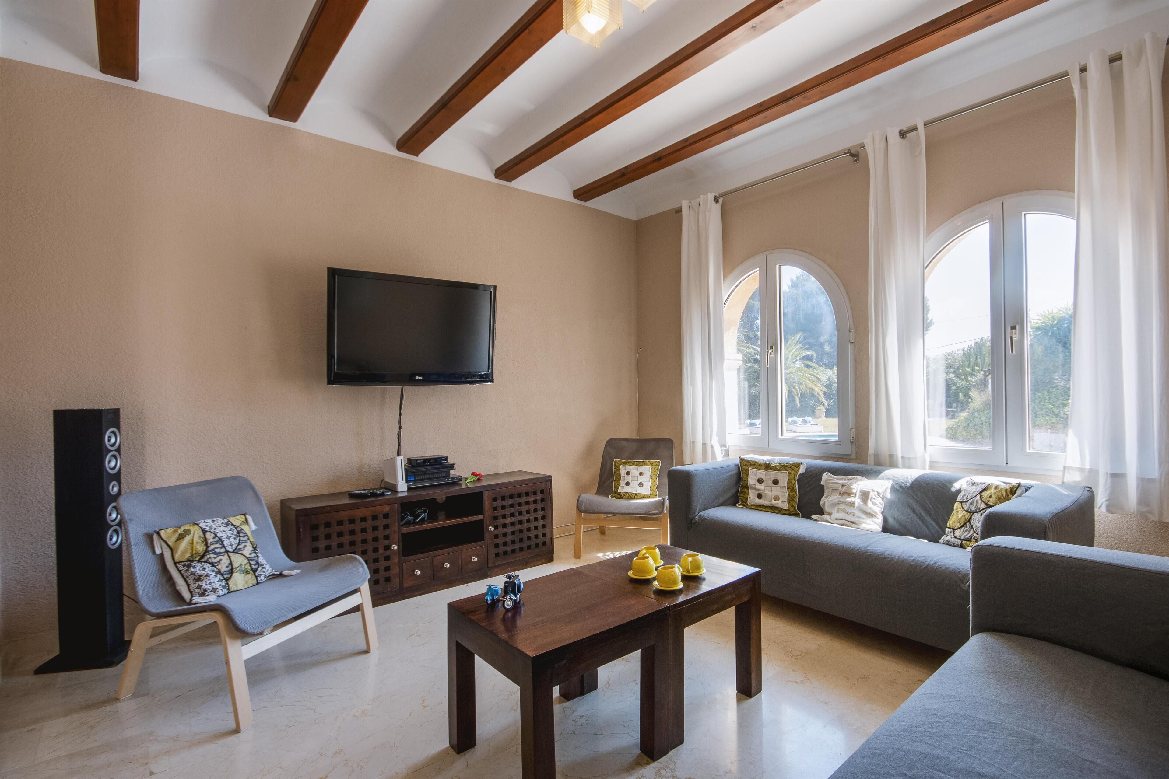 A living room with a sofa, a chair, a coffee table, a TV, and a window with curtains.