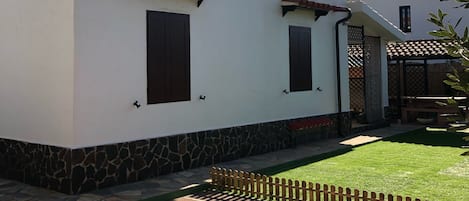 A two-story house with a white exterior, stone foundation, and a small garden area with a wooden fence.