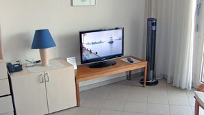 Una habitación de hotel con una televisión sobre una mesa de madera, una lámpara de escritorio, un teléfono y un armario.