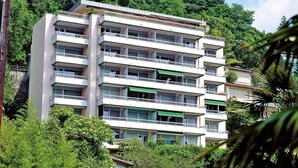 Un edificio de varios pisos con balcones, rodeado de abundante vegetación.