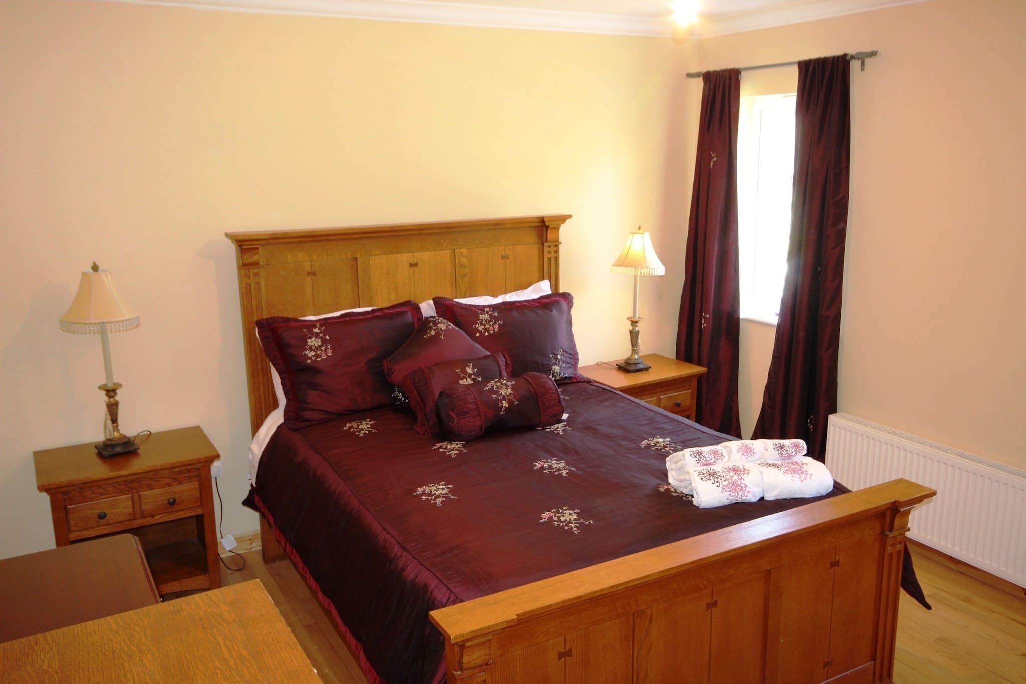 A neatly made bed with a wooden headboard, a bedside table with a lamp, and a window with curtains.