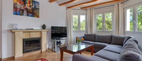 A living room with a fireplace, a flat-screen TV, a sofa, and a window with a view of trees.