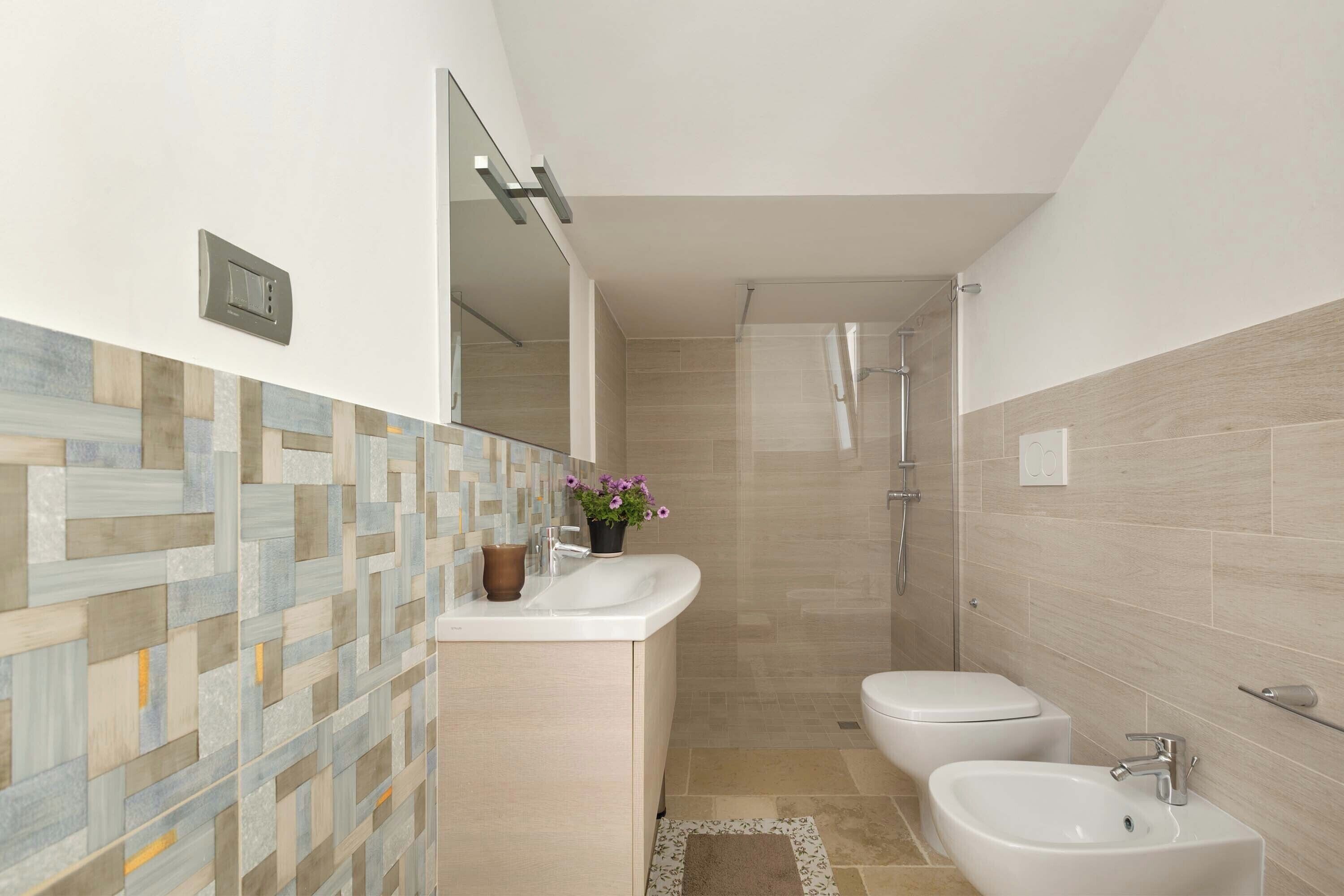 A modern bathroom with a tiled backsplash, a sink, a bidet, and a shower.