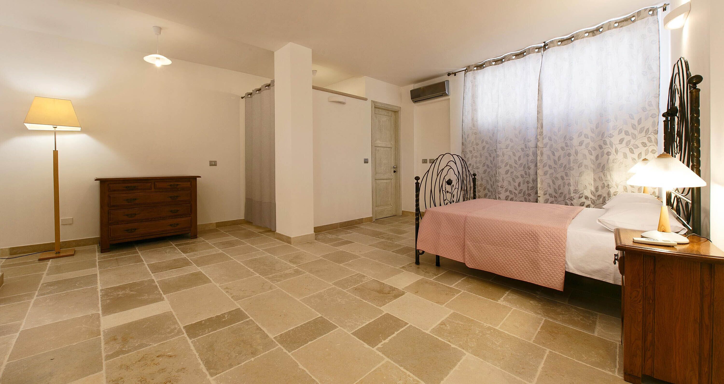 Une chambre à coucher avec un lit, une commode, une table de chevet, une lampe et un rideau.