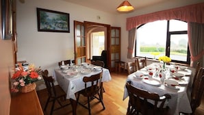 A dining room with a table set for six, wooden chairs, a chandelier, a painting on the wall, and a view through a window. - Pooreen House offering views of the Atlantic Ocean (Inverin)