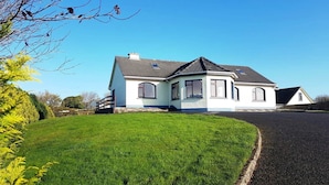 A single-story house with a sloped roof, a front porch, and a well-maintained lawn. - Pooreen House offering views of the Atlantic Ocean (Inverin)
