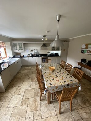 A spacious kitchen with a dining area, featuring a large island, wooden chairs, and a patterned tablecloth.