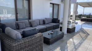 Un espace de vie extérieur moderne, avec un canapé gris, des meubles en osier et une table basse en verre.