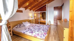 A bedroom with a wooden ceiling, a bed with floral bedding, a bedside table, a wardrobe, and a door leading to another room.