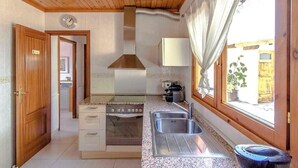 A compact kitchen with a stove, sink, and window overlooking a courtyard.