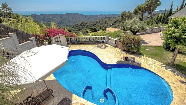 A swimming pool with a view of the sea, surrounded by a stone deck and a wooden fence.