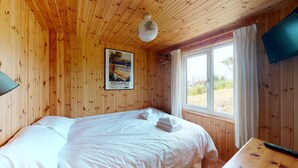 A wooden-paneled room with a bed, a poster on the wall, and a window with curtains. - F67 Ischia, Riviere Towans (Hayle)