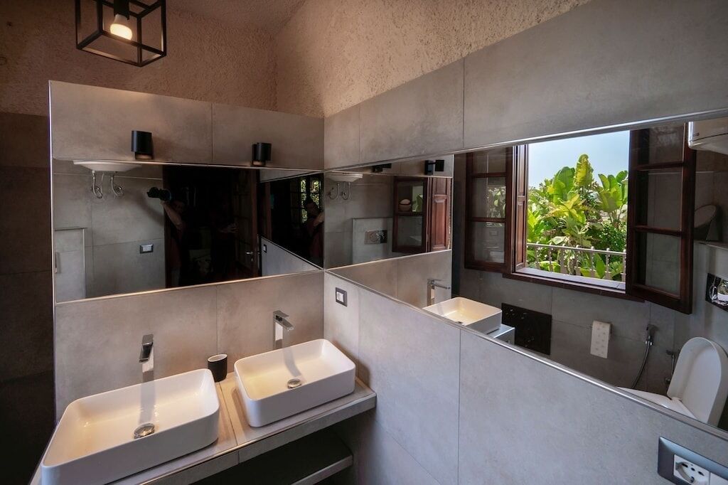 A modern bathroom with two sinks, a large mirror, and a window providing a view of greenery.