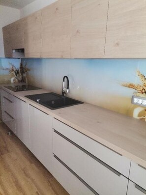 Eine moderne Küche mit hellen Holzschränken, einer schwarzen Spüle und einem Strauß getrockneter Blumen auf der Arbeitsplatte.