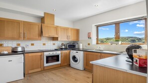 A modern kitchen with wooden cabinets, a built-in oven, a microwave, and a washing machine.