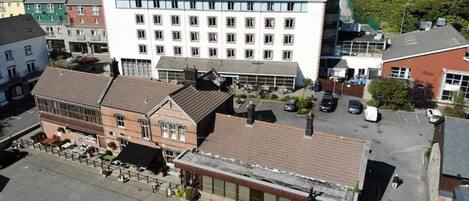 A multi-story building with a flat roof, a parking area, and a small outdoor seating area.