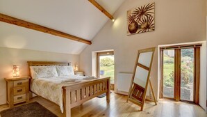 A bedroom with a wooden bed, bedside tables, a radiator, and a large window with a view of the outdoors. - 2 Bed in Tiverton (oc-cide) (Cove)