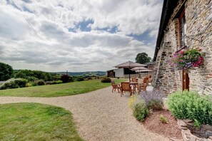 A stone building with a gravel path leading to an outdoor seating area with tables and chairs.