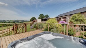 A hot tub on a wooden deck with a view of a stone building and surrounding greenery. - 2 Bed in Tiverton (oc-cide) (Cove)