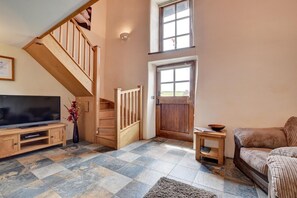 A spacious living area with a wooden staircase, a flat-screen TV, a wooden coffee table, and a comfortable sofa.