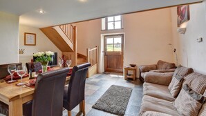 A dining area with a wooden table set for four, a sofa, and a staircase leading to a door. - 2 Bed in Tiverton (oc-cide) (Cove)