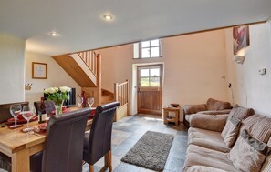 A dining area with a wooden table set for four, a sofa, and a staircase leading to a door.