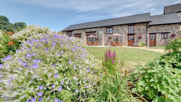 A stone building with a grassy lawn, outdoor seating, and flowering plants. - 2 Bed in Tiverton (oc-cide) (Cove)