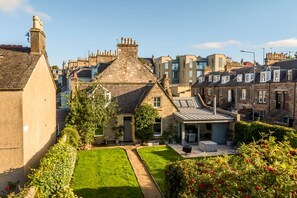 A residential area with stone houses, a well-maintained lawn, and a clear sky.