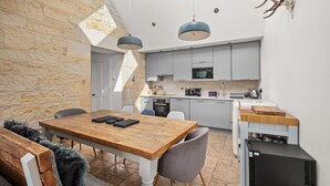 A modern kitchen with grey cabinets, a wooden dining table, and pendant lighting. - Stylish 4‑Bedroom St Andrews Cottage with Private Garden, Parking & Walk to South Street (St. Andrews)
