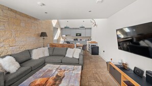 A modern living room with a stone wall, a grey sofa, a wooden coffee table, and a flat-screen TV. - Stylish 4‑Bedroom St Andrews Cottage with Private Garden, Parking & Walk to South Street (St. Andrews)