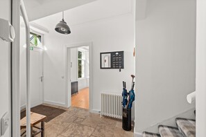 Un passadís amb un radiador, un penjallots amb paraigües i una porta que dona a una altra habitació.
